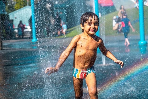 Happy muddy child playing and running through jets of water in a playground water park fountain in