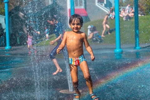 Happy child playing and running under the water jets of a splash pad in vancouver, british