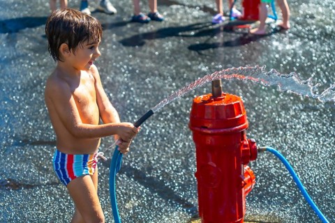 Happy child spraying water with a fire hydrant during a hot summer day in vancouver, british