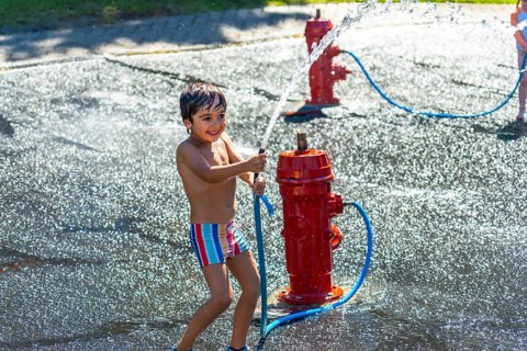 Happy child playing and splashing with water jets coming out of a small red fire hydrant during a