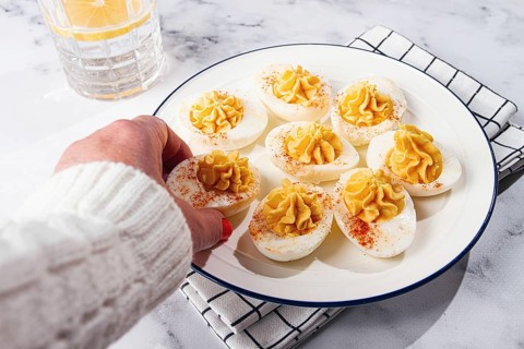 Stuffed eggs with paprika, on a plate, a woman's hand reaches for it