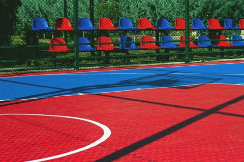 A vibrant basketball court features a mix of red and blue colors. Empty seats line the side,