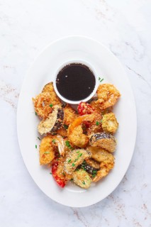 Shrimp and assorted vegetables are deep fried in a light batter and served on a white plate. A