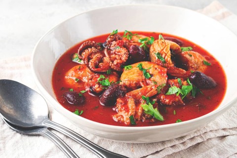 Seafood assortment in tomato sauce, olives, in a white plate