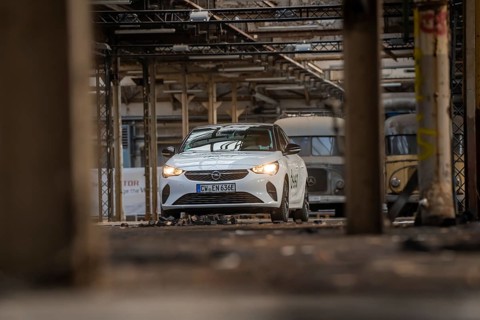 A white Opel with car sharing logo stands between other vehicles in an old industrial building,