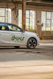 A white car with car sharing logo is parked in a hall with large windows, Deer E-Car Sharing,