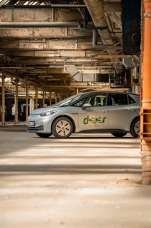 A car with the car sharing logo is parked in a light-flooded industrial building, Deer E-Car