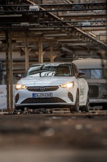 White Opel with car sharing logo in an urban industrial building with visible metal structures,