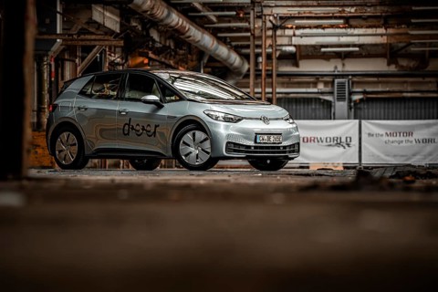 An electric vehicle is parked in an empty, urban factory building with visible pipes and