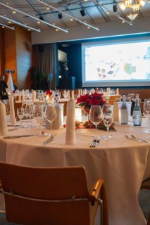 An elegant banquet hall with festively decorated tables and a projection screen in the background,