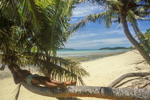 Boy lying on a coconut tree on the beach of Tavewa Island, Yasawa Islands, Fiji