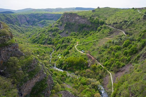 Lush green gorge with winding paths along which a river flows, surrounded by mountains, Dashbashi