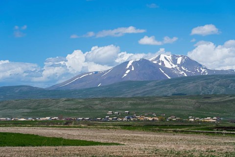 View of snow-capped mountains behind vast fields and a village, landscape near Satche, Mount Didi