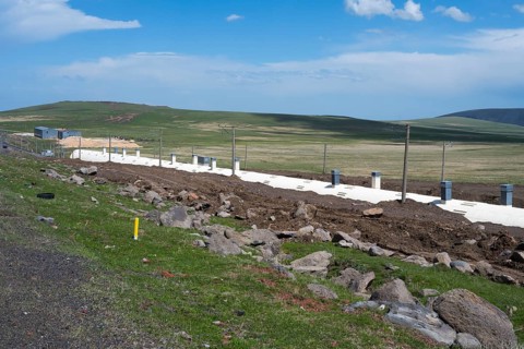 Wide landscape with green field and blue sky, in the foreground a road and a covered railway track,
