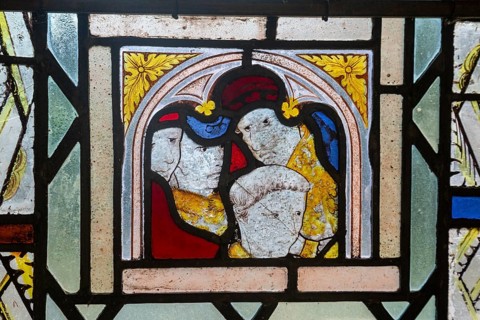 Close-up of medieval style stained glass showing faces of people, Ufford church, Suffolk, England,