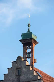 A historic bell tower with bell and weather vane against a clear blue sky, Engelberg near
