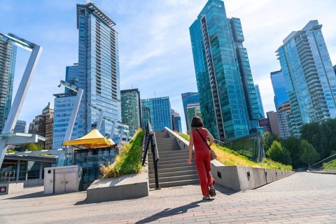 Tourist walking up stairs in downtown vancouver with modern skyscrapers, green roof and blue sky in