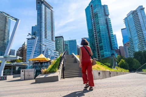 Young woman tourist walking up stairs in a modern city park with skyscrapers and office buildings