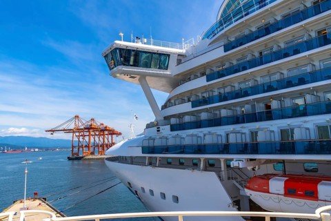 Large white cruise ship docking in vancouver harbor, surrounded by towering cargo cranes and