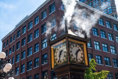 Steam clock releasing vapor against a backdrop of a red brick building and a bright blue sky,