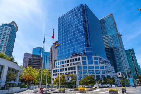 Modern skyscrapers rising against a blue sky, with canadian and pride flags waving in the