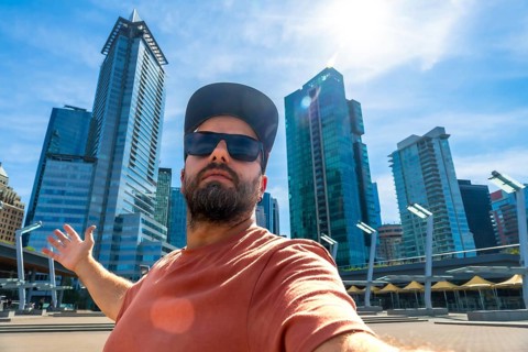 Happy bearded tourist wearing sunglasses and a baseball cap is taking a selfie with outstretched