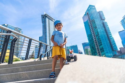 Young boy standing on steps playing with a toy car, with vancouver's modern buildings and clear