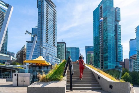 Businesswoman climbing stairs in a green urban space with skyscrapers in the background in