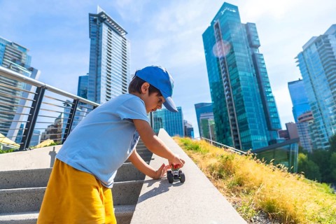 Young boy playing joyfully with a toy car on the steps of an urban park, soaking up the warmth of a