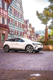 White car in an old town with magnificent half-timbered buildings and a statue, Deer E-Carsharing,