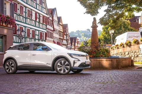 White Renault parks at a fountain in a picturesque old town, Deer e-Carsharing, Renault Megane,