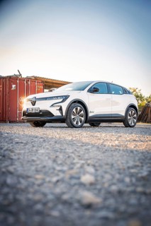 A white electric car stands in front of a container on a gravel field at dusk, Deer E-Carsharing,