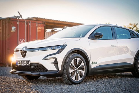 A white electric car stands on a gravel field in front of a container at dusk, Deer E-Carsharing,