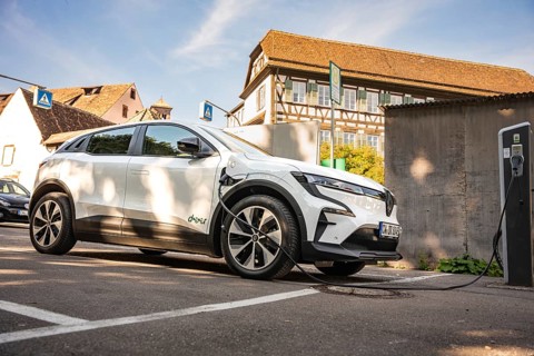 A white electric car charges at a station next to a half-timbered house in a parking lot, Deer