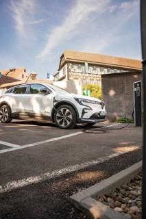 Car at a charging station in front of a half-timbered house in a sunny parking lot, Deer