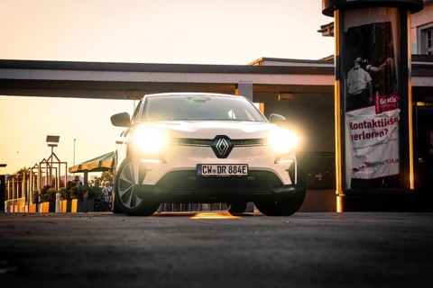 Car with bright headlights in an urban environment at night in front of posters, Deer E-Carsharing,