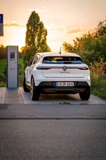 An electric car is connected to a charging station surrounded by the setting sun, Deer