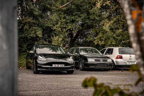Parking lot with black cars surrounded by thick vegetation, deer e-car sharing, Tesla Model 3,