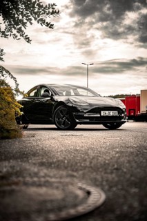 Black car in a parking lot under cloudy sky with trees nearby, Deer E- car sharing, Tesla Model 3,