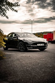 Black car on an empty side of the road surrounded by trees and a cloudy sky, Deer E- car sharing,