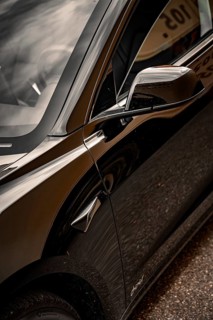 Close-up view of the side mirrors and body of a black car with shiny surface, Deer E-Carsharing,