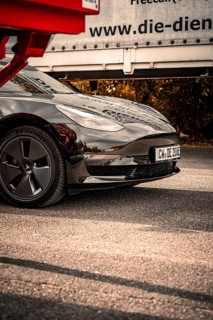Close-up of a black car with shiny paint and visible reflection on the asphalt, Deer E-Carsharing,
