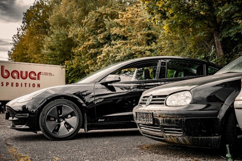 Black car and older vehicle in a parking lot with a truck in the background, Deer E-Carsharing,