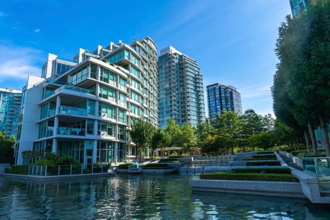 Modern glass and concrete buildings stand tall, reflecting in the calm water of a city park,