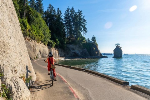 Tourist is enjoying a sunny day riding a bicycle along the stanley park seawall, with the iconic