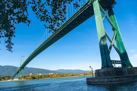 Lions gate bridge extending over burrard inlet with stanley park seawall in foreground and north