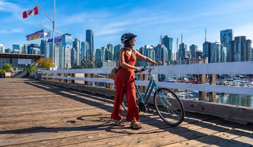 Female tourist wearing a helmet is walking alongside her bicycle on a wooden pier, enjoying the