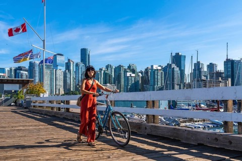 Female tourist walking with her bicycle on a wooden pier, enjoying vancouver downtown skyline in