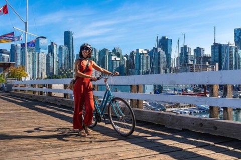 Young woman walking alongside her bicycle on a vibrant pier, soaking in the stunning cityscape of