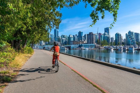 Tourist riding bicycle on the seawall in stanley park enjoying the scenic view of the vancouver